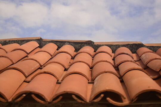 Telhado de telhas vermelhas no topo de uma casa brasileira com c&eacute;u azulado e nuvens suaves ao fundo