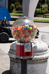 Close-up of a vintage red gumball machine filled with colorful bouncy balls on a sunny day in a...