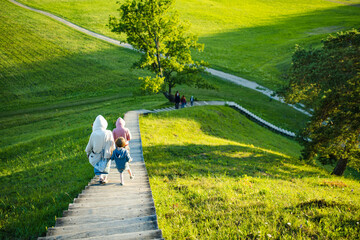 Three kids descend a long wooden staircase surrounded by rolling green hills at the Kernave...