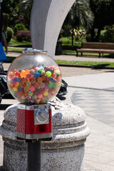 Close-up of a vintage red gumball machine filled with colorful bouncy balls on a sunny day in a...