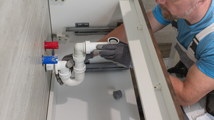 Fototapeta premium Installation of bathroom furniture. The plumber's hands is connecting a siphon to a waste pipe.