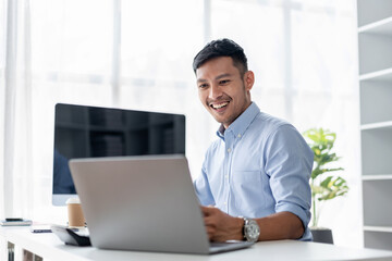 Smiling Adult Asian Man Working on Laptop at Bright Office Desk - Business Professional Happy at...