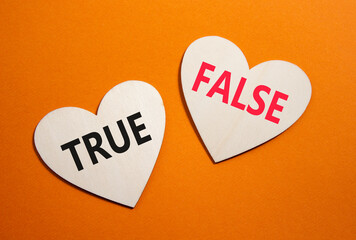 True or False symbol. Concept word True or False on wooden hearts. Beautiful orange background....