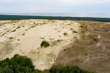 Aerial view of rolling sand dunes meeting dense green forest at the Curonian Spit in Lithuania, creating a stunning contrast of landscapes by the Baltic Sea.