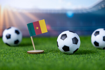 Cameroon national flag and miniature soccer balls resting on artificial green grass with a stadium background, representing African football and international sport championship spirit
