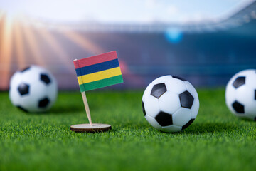 Miniature national flag of Mauritius with soccer balls on green grass, symbolizing global football competition and national team spirit in a stadium