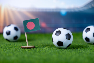 Vibrant miniature Bangladesh flag stands on green artificial turf amidst small soccer balls, symbolizing national team pride, international sport, and global football competition
