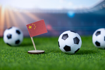 Small Chinese flag with soccer balls on green stadium turf, symbolizing global football competition, national team events, and sports pride