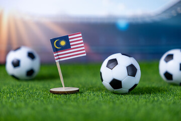 Malaysian flag stands proudly with soccer balls on green grass in a stadium, representing national pride, sports championship, and international competition
