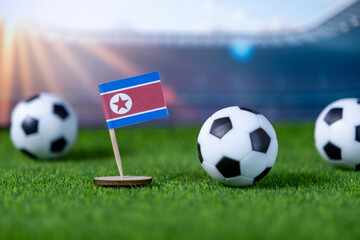 Miniature North Korean flag and small soccer balls on vibrant green grass, symbolizing global football tournaments and national sports representation within a stadium