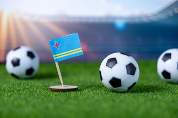 Aruba flag proudly stands with soccer balls on a green pitch, symbolizing international football competition and national team spirit in a stadium