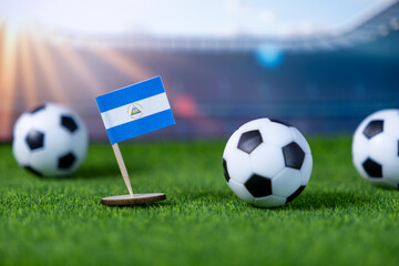 Small Nicaraguan flag and soccer balls on green grass with stadium background, symbolizing national pride in sports and international competition