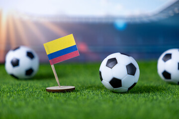 Miniature Colombian flag and black-and-white soccer balls resting on lush green artificial turf,...