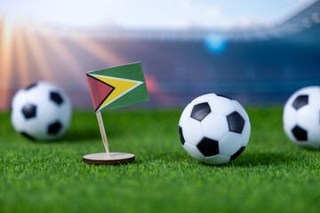 Guyana flag stands proudly on green soccer turf with miniature footballs and a stadium background, symbolizing national sports pride and international competition