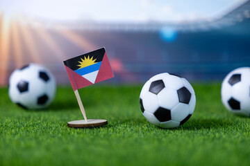 Antigua and Barbuda's national flag proudly stands with soccer balls on lush green grass, symbolizing Caribbean national team spirit and global football competition