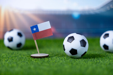 A Chilean flag stands on artificial grass with miniature soccer balls, representing national pride for international football championships in a stadium environment