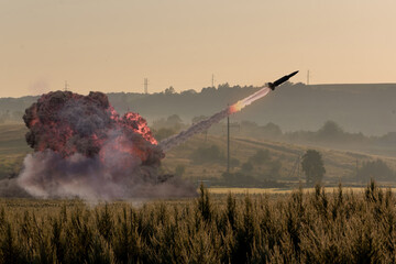 Launching a military rocket in the field - a trail of fire in the sky and puffs of smoke from the launch in the morning landscape.