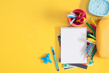 School stationery on yellow background with copy space, open notebook, pencil case, alarm clock...