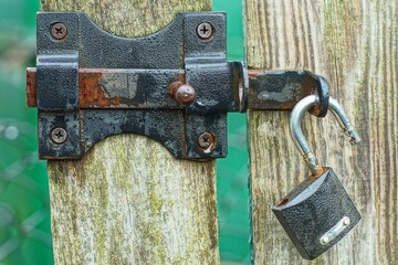 one iron black rusty open new modern screwed industrial latch with safe small padlock on bracket on grey wooden gate day outside