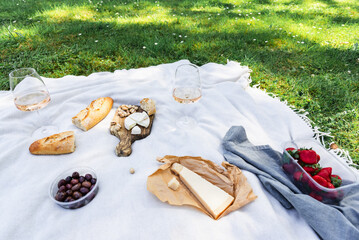 Two glasses of rose wine with snacks on a blanket on the grass in the park. Summer picnic. Alcohol. Public places.