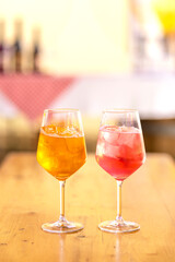 Glasses of pink and yellow alcoholic drink Aperol Spritz with ice on table on warm day. Celebration with glasses of refreshing fruity soft drink