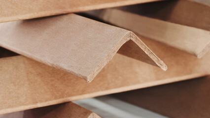 Stack of cardboard corner protectors for packaging, corners are brown and arranged in a row as...