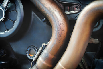 A pair of bronze motorcycle exhaust pipes. The pipes are curved and exit from the engine.