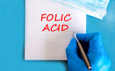 Folic acid symbol. Concept words Folic acid on beautiful white note. Doctor's hand in blue medical...