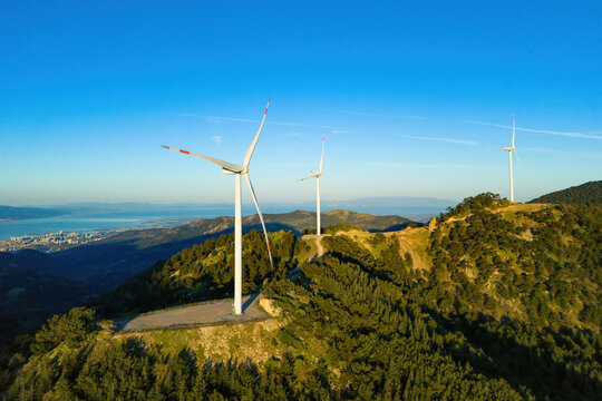 Wind turbines in the wind energy farm in mountain with city on background. Aerial view. Energy transition with wind power farm - Powered by Adobe