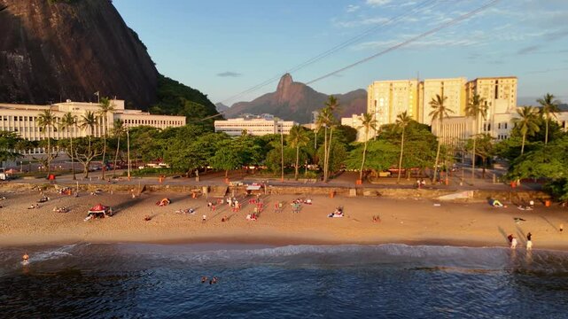 Golden Sunrise Over Praia Vermelha in Urca, Rio de Janeiro, Brazil with Early Morning Beachgoers and Dramatic Mountain Backdrop