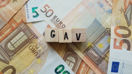 GAV acronym made of wooden letter cubes on pile of Euro banknotes. Garantie Accidents de la Vie...