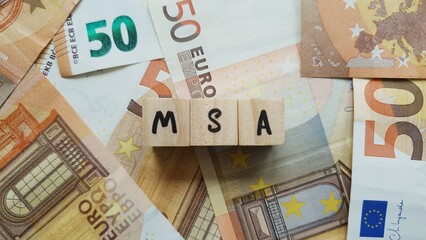 MSA acronym made of wooden letter cubes on pile of Euro banknotes. Mutualité Sociale Agricole (Agricultural Social Security Fund)