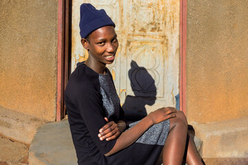 village single young african woman wearing a beanie standing in front of the house , in the yard, wide portrait