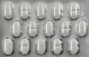 Closeup view of a silver pack containing white capsules, sealed in transparent plastic. Pharmaceutical medication in protective packaging, commonly used for supplements, antibiotics, or pain relief.