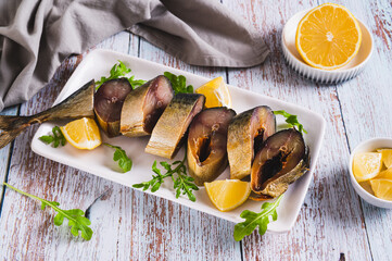 Smoked mackerel, lemon slices and herbs on a plate on the table