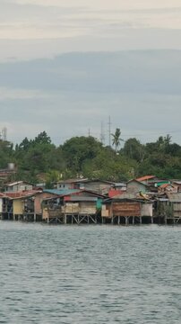Vertical video. Makeshift homes line the coast in Lapu-Lapu near city buildings and ocean