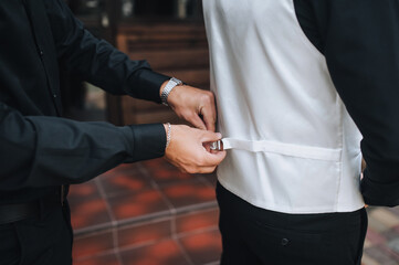 Young businessman man helps, fastens clothes with his hands to the groom in the morning. Wedding photo.