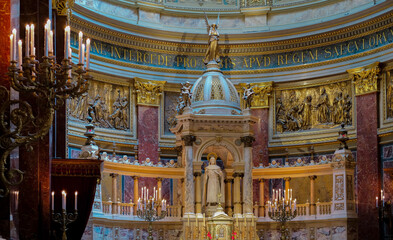 Grand church altar with statue of Christ, golden reliefs, and domed baldachin. Marble steps and candle holders frame the sacred scene. © olga