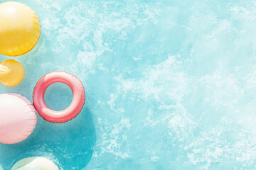 Summer composition with pastel inflatable rings and balls floating on turquoise textured background with copy space. For seasonal designs, vacation ads, beach party visuals, playful lifestyle themes