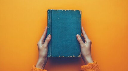 Hands holding vintage teal book on yellow background.