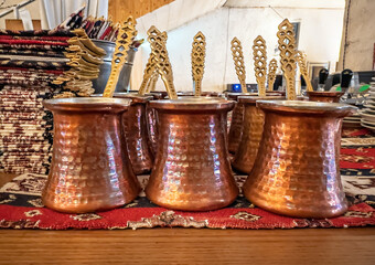 Traditional hammered copper Turkish coffee pots (cezve) with ornate brass spoons, displayed on a...