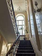 Elegant Interior of a Luxury Home with a Marble Staircase and a Large Arched Window. Grandeur of Classical Architecture: A Majestic Stairway with Marble Steps and Ornate Wrought Iron Railing