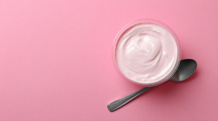 Pink background showcasing yogurt in a plastic cup with spoon, top view with space for text