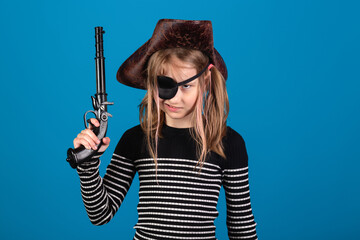 Young cute european pirate girl in hat and eye patch with old pistol or gun against blue background