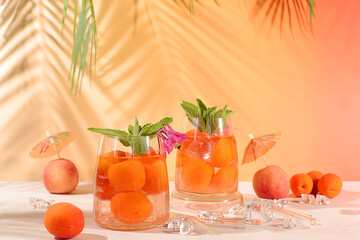 Iced peach tea or cocktail with mint and apricots, refreshing summer drink recipe. Two glasses with...