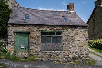 Rustic stone cottage with boarded windows and sagging roofline a weathered green painted door.