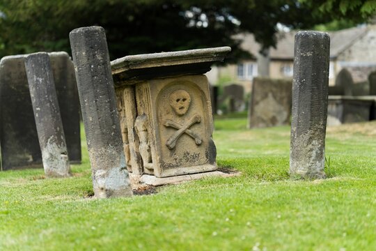 Eyam village Derbyshire UK. Ancient gravestone with skull and crossbones in a lush green cemetery.