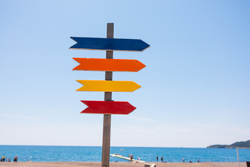 Wooden beach signpost with arrows on seaside promenade, copy space. Summer vacation, coastal...