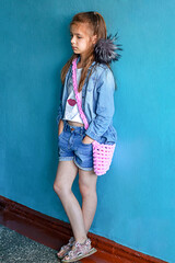 Casual portrait of a young girl in denim outfit against blue wall