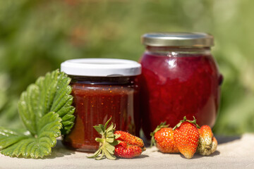 Homemade strawberry preserves in glass jars between green leaves